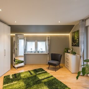 Modernes Schlafzimmer mit großem Kleiderschrank, Sessel, Pflanzen und viel Tageslicht.