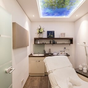 Moderner Behandlungsraum für Kosmetik und Wellness mit Liege und Naturmotiv an der Decke.